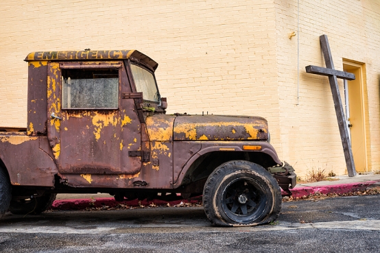 Rusted jeep with a flat tire sits outside the Capitol Restoration shop where a wooden cross leans against the door. The salvage shop serves at the Triple Crown Cowboy church on Thursday nights and Sunday mornings in Frankfort, Kentucky, USA.