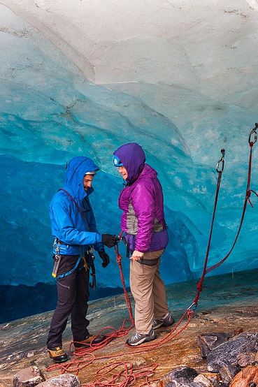 Guide attachs rope to harness of senior woman preparing to rappel into an ice cave on Lemon Glacier, Juneau Icefield, Juneau, Alaska, USA