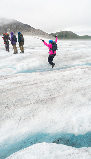 Woman jumps over a small crevasse during a trekking adventure on Lemon Glacier, Juneau 