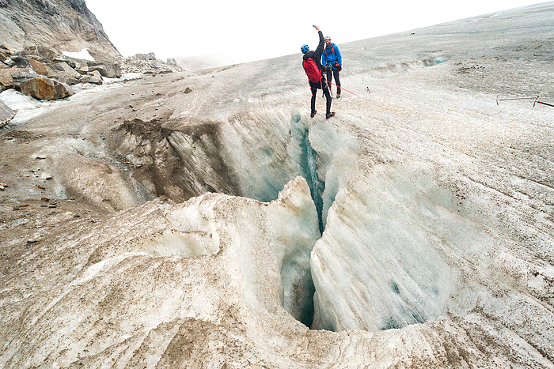 Guide spots a hikers who leans back over a deep crevasse on Lemon Glacier, Juneau Icefield, Juneau, Alaska, USA