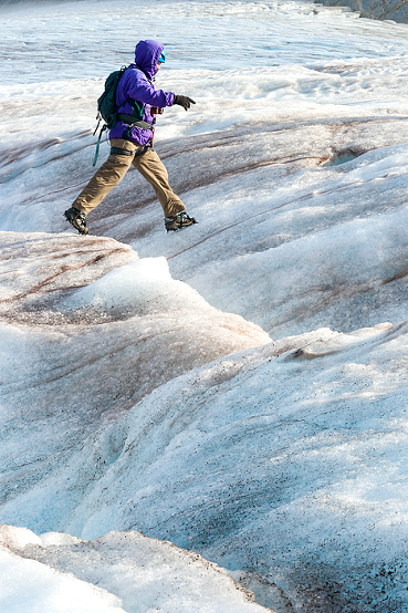 Woman jumps over a crevasse on Lemon Glacier, Juneau Icefield, Juneau, Alaska, USA