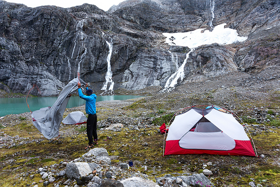 Campsite of tent in glacier valley with mineral lake and waterfall at Lemon Glacier, Juneau Icefield, Juneau, Alaska, USA