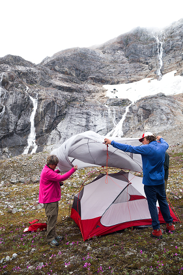 Senior woman and male guide in 20s set up tent for overnight camp, Lemon Glacier, Juneau, Alaska