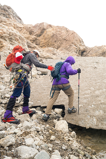 Guide helps a woman step up from boulders onto the ice on a trekking adventure on Lemon Glacier, Juneau Icefield, Juneau, Alaska, USA