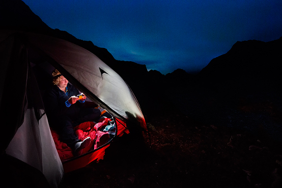 Woman looks her camera inside a tent at night with faint Northern Lights 