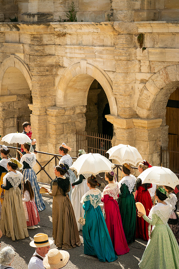 Fete du Costume passing by the ancient Roman Arena. Over 500 women dress in traditional attire from their region depicting differing lace and hats in this annual summer festival, Arles, France, Europe